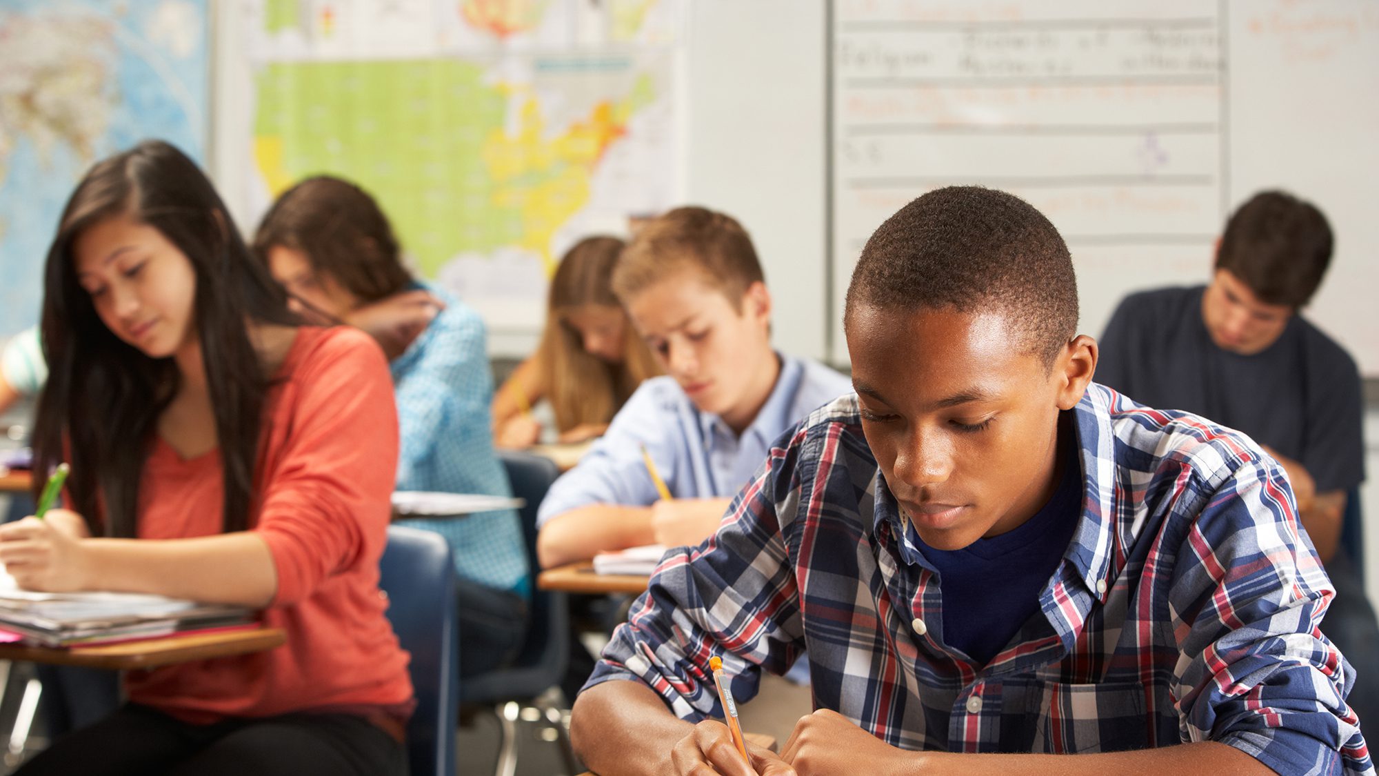 Male Pupil Studying At Desk In Classroom